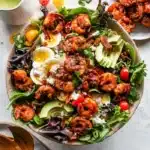 A vibrant Jerk Shrimp Cobb Salad Recipe served in a pink bowl with fresh dressing drizzled on top.