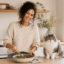 Maya Collins preparing a fresh salad in her bright kitchen while Mochi sits beside her