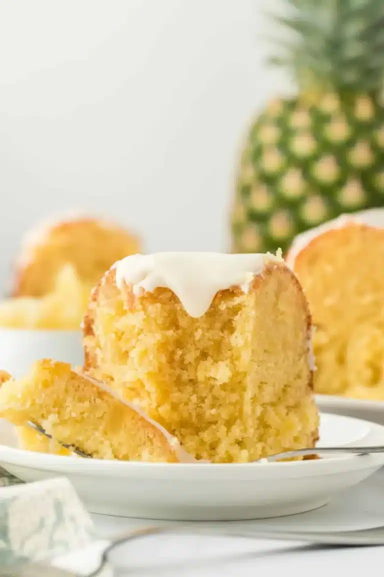 A slice of Pineapple Pound Cake Recipe on a white plate with a fork, showing its moist interior and glaze