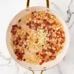 Fried Cabbage Recipe step one: sautéed bacon, onions, and garlic in a skillet on a marble countertop