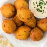 Golden fried hush puppies resting on a paper towel with a dipping sauce ramekin