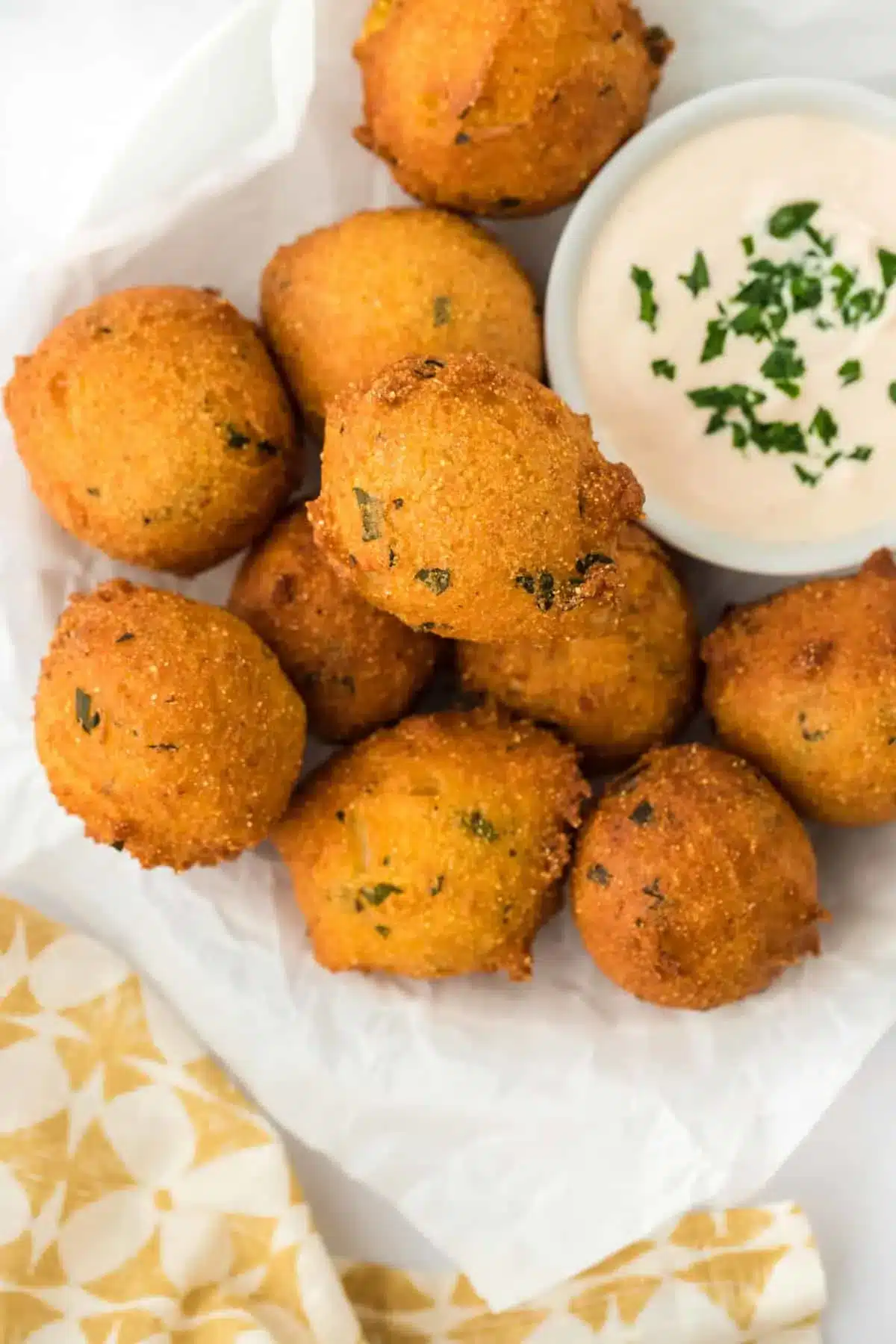 Golden fried hush puppies resting on a paper towel with a dipping sauce ramekin