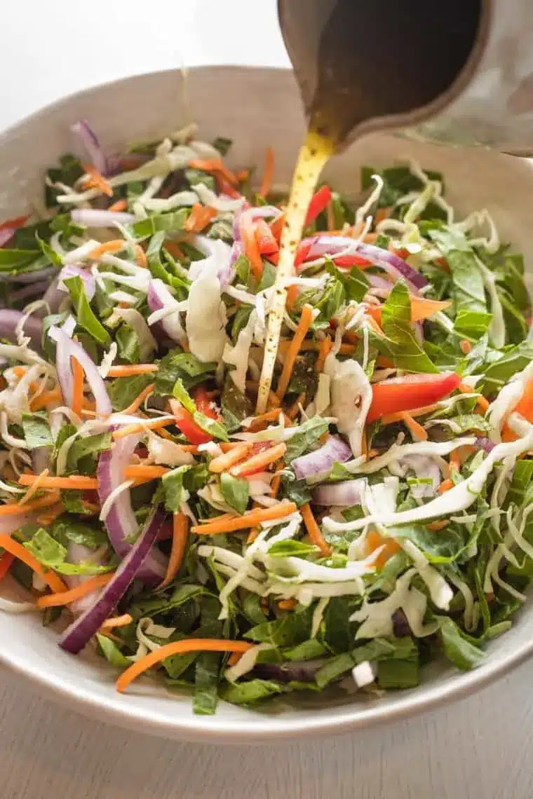 Vinaigrette dressing being poured over vegetable slaw