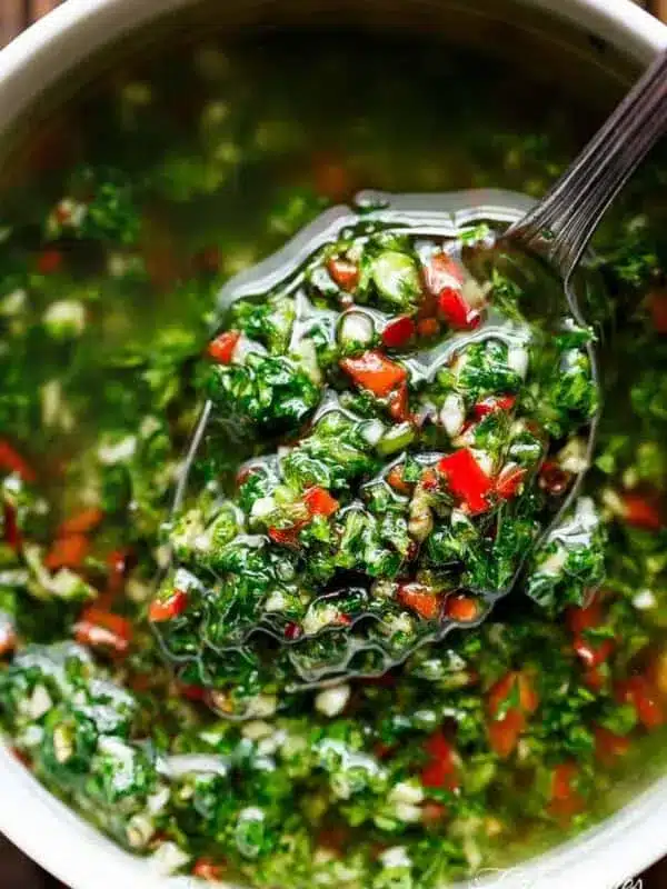 A spoon lifting vibrant chimichurri with green herbs and red chili pieces